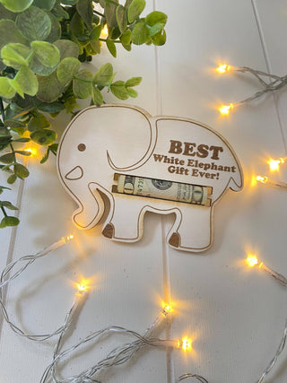 Wooden elephant money holder engraved Best White Elephant Gift Ever with a rolled bill, styled with string lights and greenery