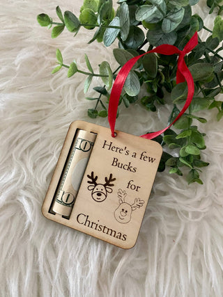Here's a Few Bucks for Christmas wooden ornament with a rolled bill and red ribbon on white fur