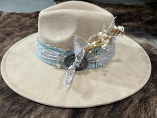 Tan felt flat brim western hat with frayed denim band, silver concho, print fabric bow and dried florals, front side view