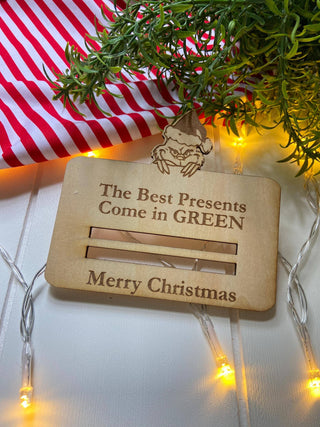 Wooden money holder engraved with Merry Christmas, shown empty with greenery
