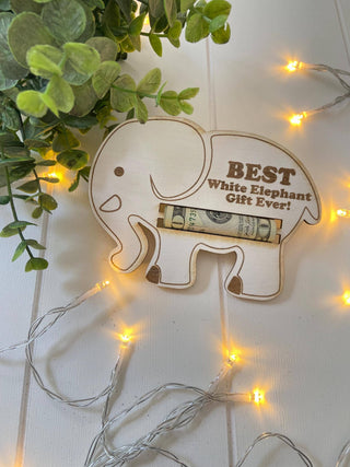 White elephant gift money holder shown with a rolled bill, greenery and string lights